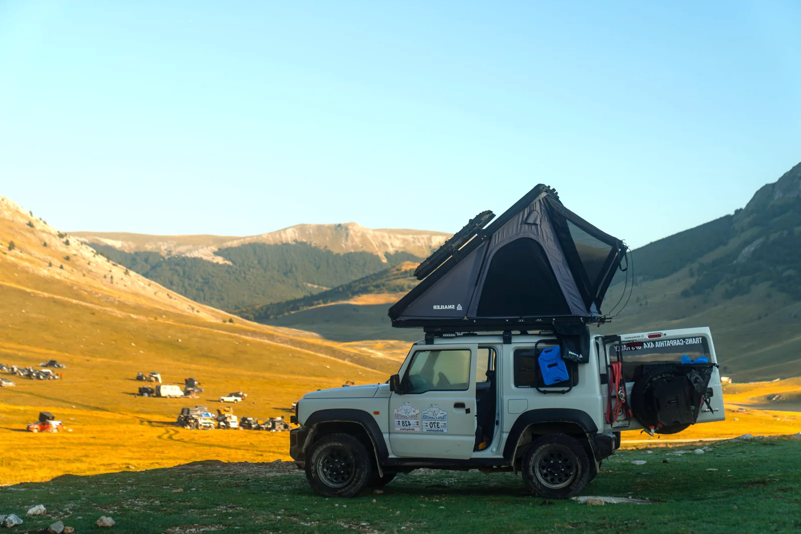 Vehicul de teren cu cortul de plafon SNAILER deschis într-un camping montan